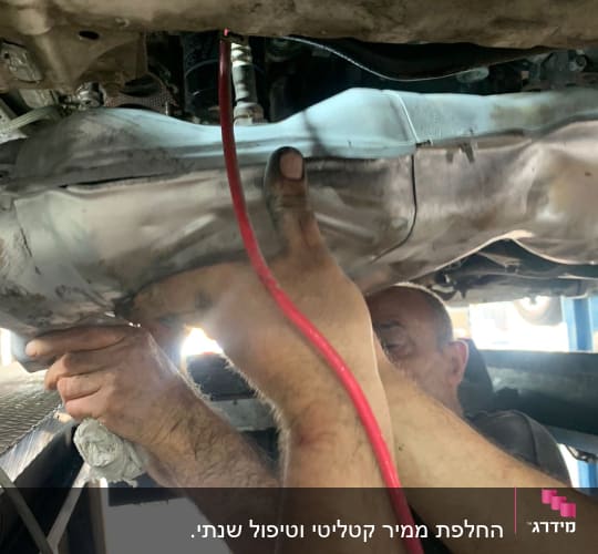 ידיים מתקנות מוסך עם צינור אדום מתחת לרכב